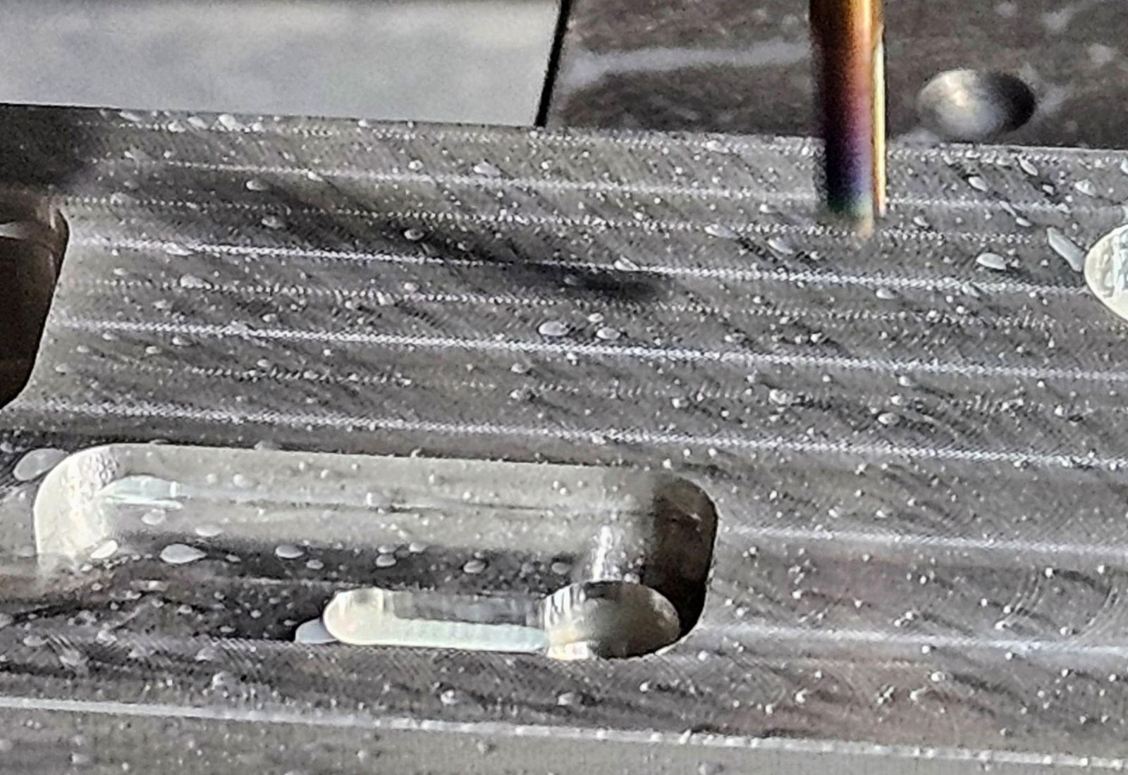 A cutter above a milled slot in an aluminum part, coolant beaded on the surface