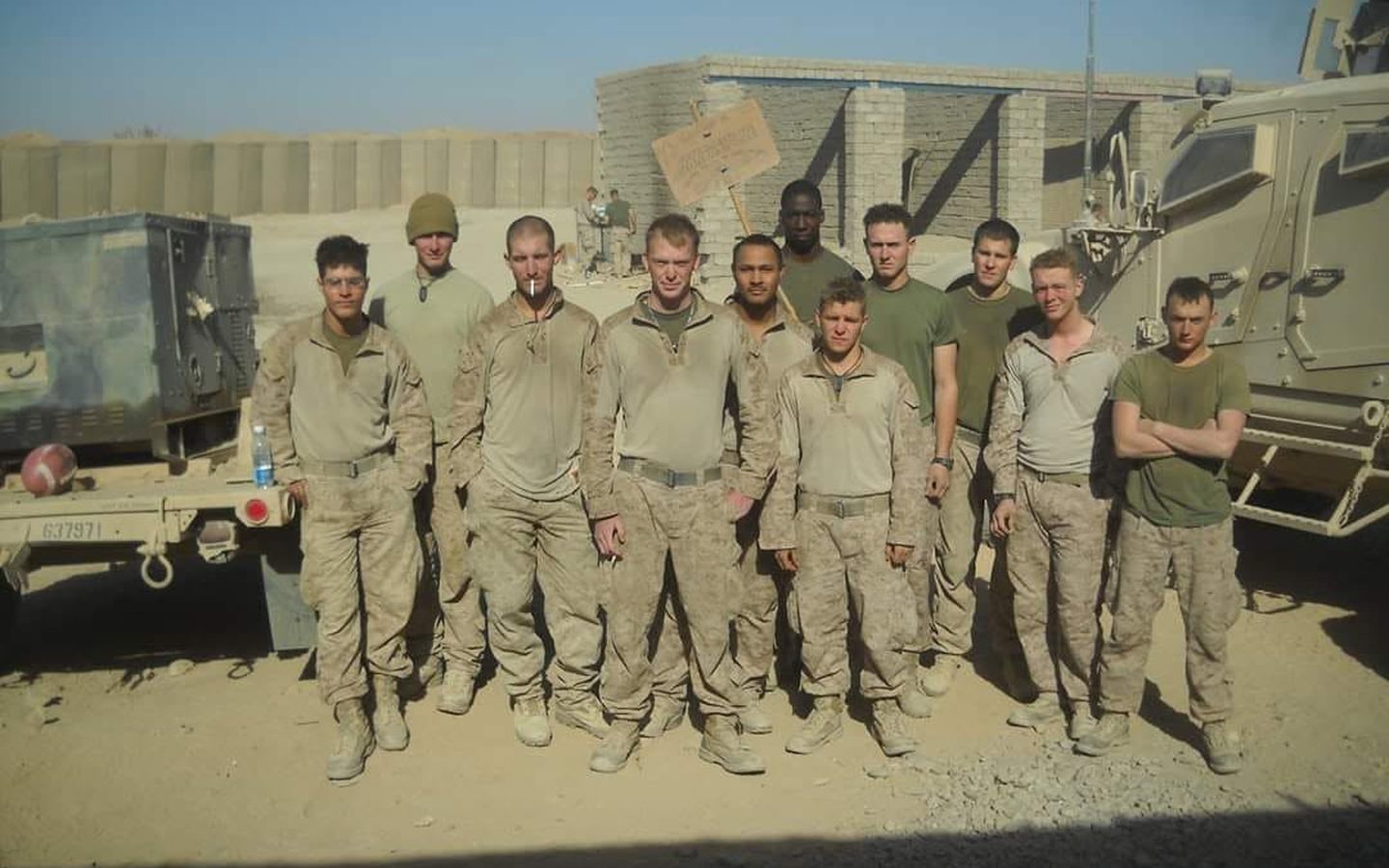 A platoon in desert uniforms lined up in front of trucks and barriers