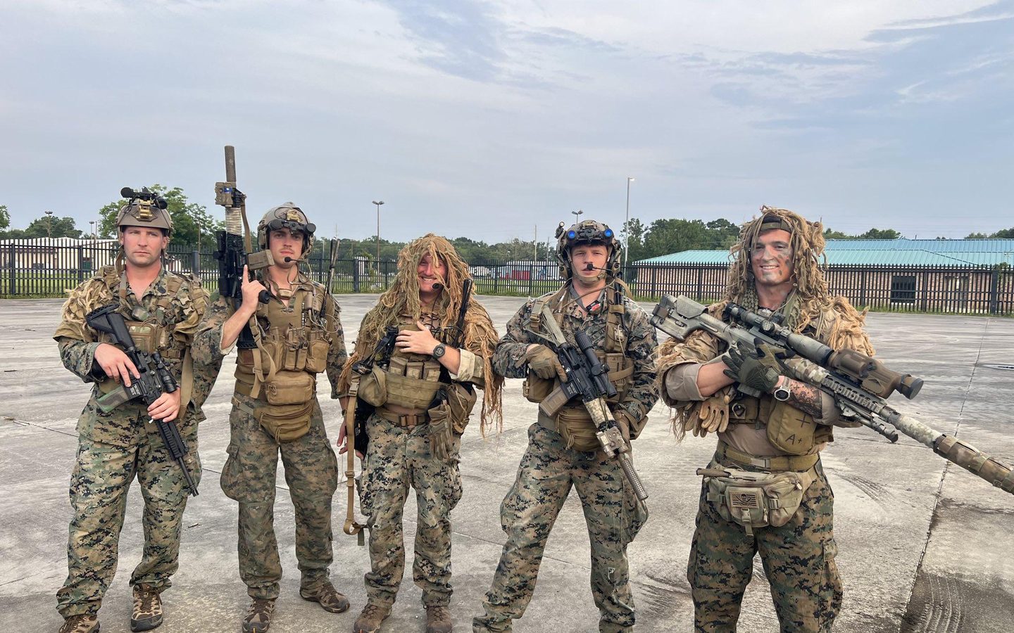 Five Marines in ghillie and plate carriers with rifles