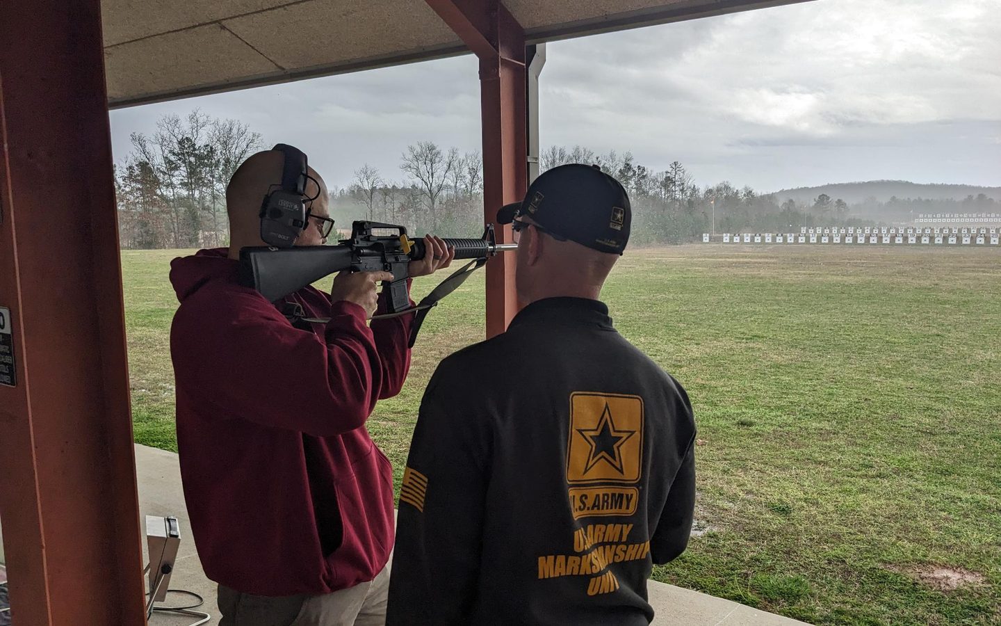 Standing with a service rifle on the firing line, a coach watching