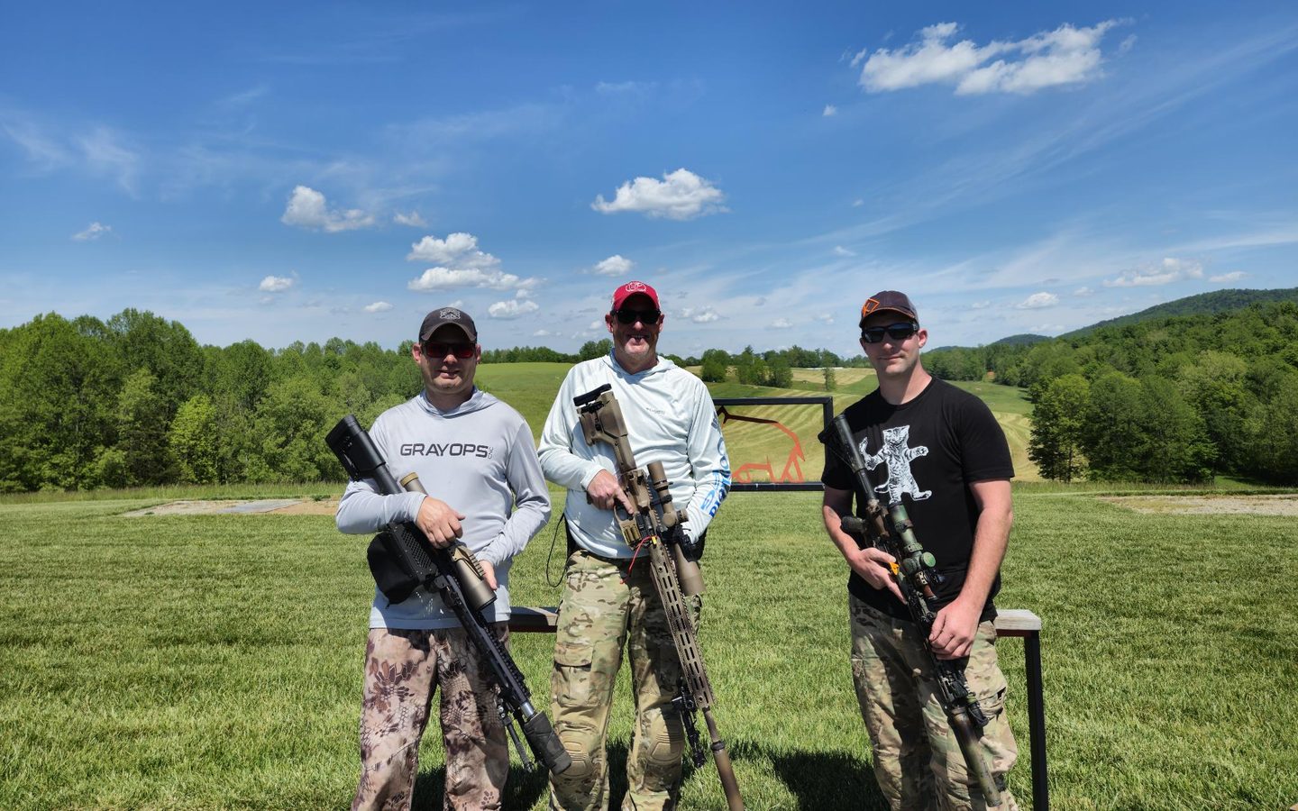Three competitors with their precision rifles on a grass range under a blue sky