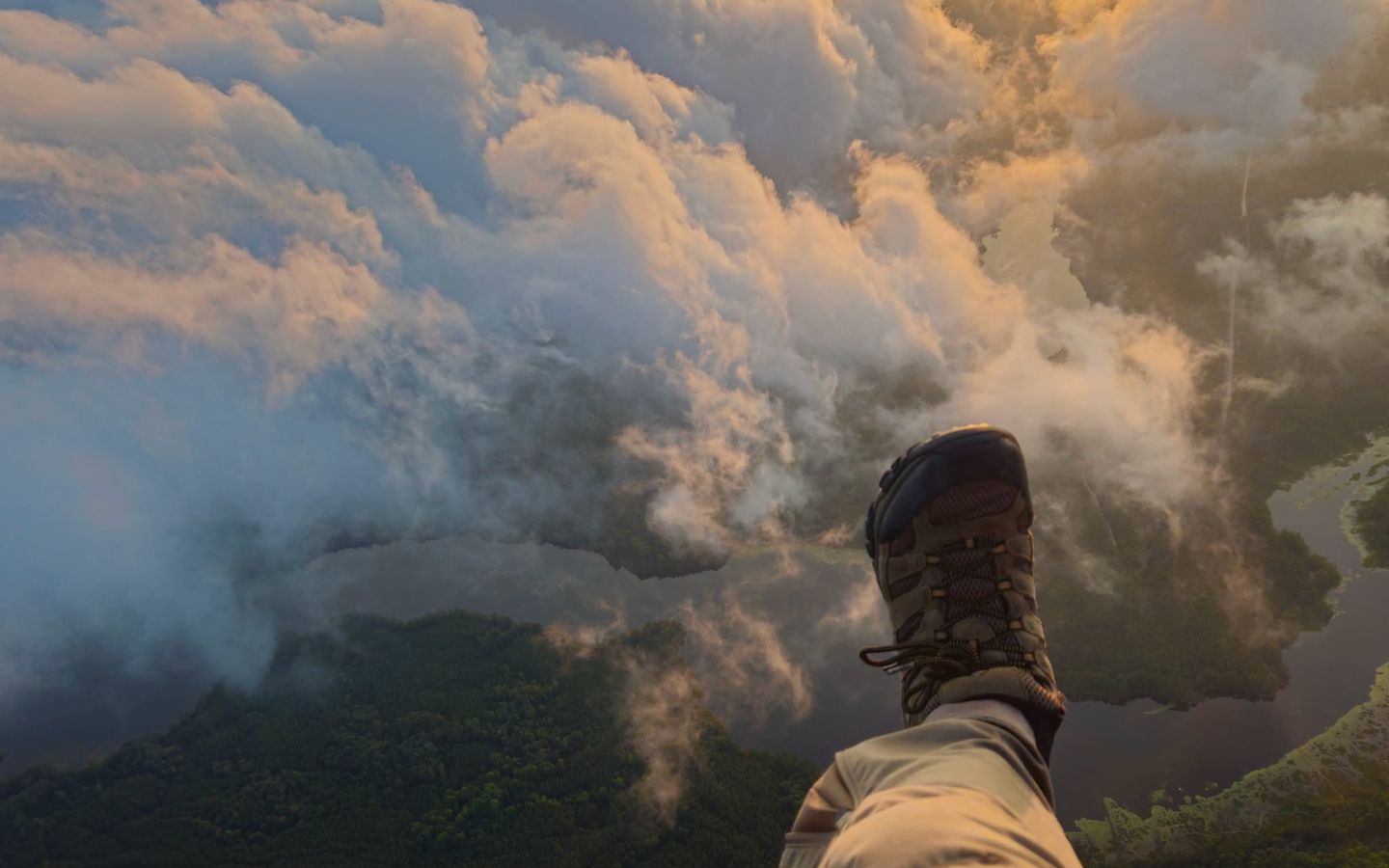 Boots dangling over a river valley, clouds below