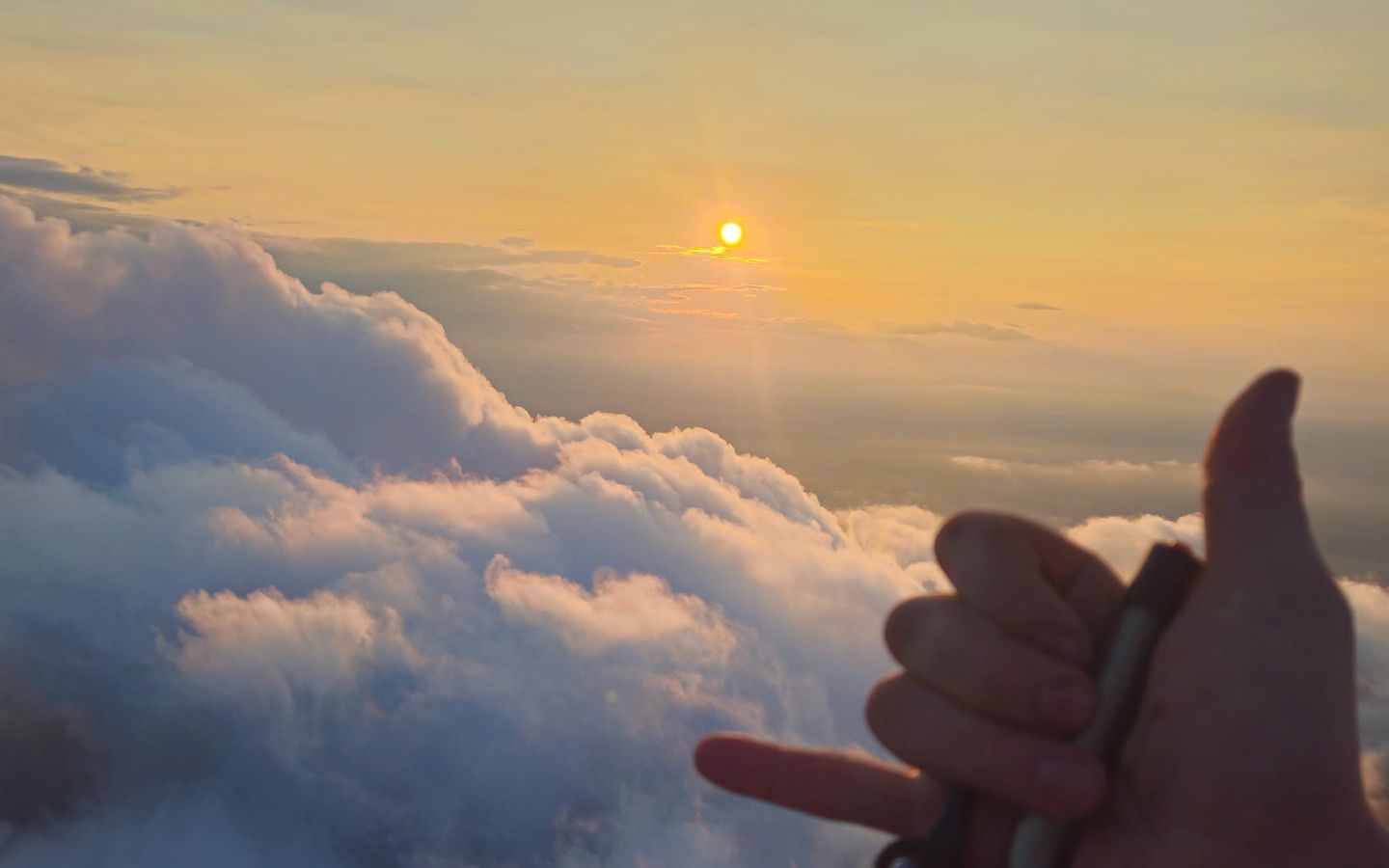 A thumbs up on the throttle above the clouds, sun low on the horizon
