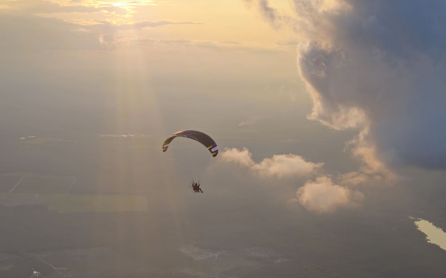 A paramotor in the evening sun over lakes and clouds
